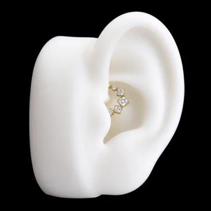 Aro clicker dorado con circones cuadrados blancos puesto en el daith de una oreja de maqueta
