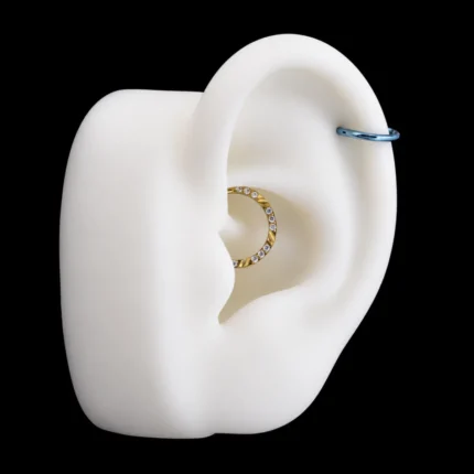 Aro clicker dorado con circones en el daith y aro azul en el hélix de una oreja de maqueta