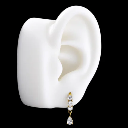 Clicker dorado con circones y gota colgante puesto en el lóbulo de una maqueta de oreja