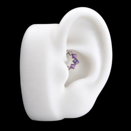 Aro clicker Sabrina plateado con circones rosa y lila puesto en el daith de una oreja de maqueta