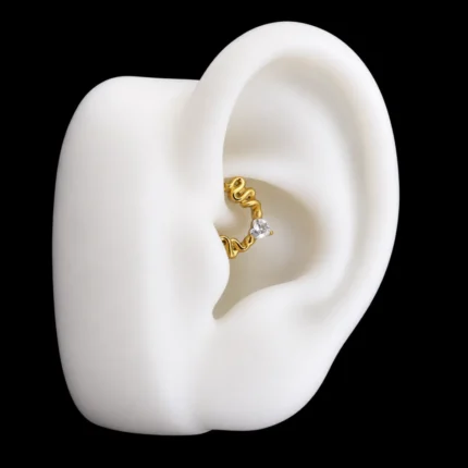 Aro clicker dorado de serpientes con corazón de circón puesto en el daith de una oreja de maqueta