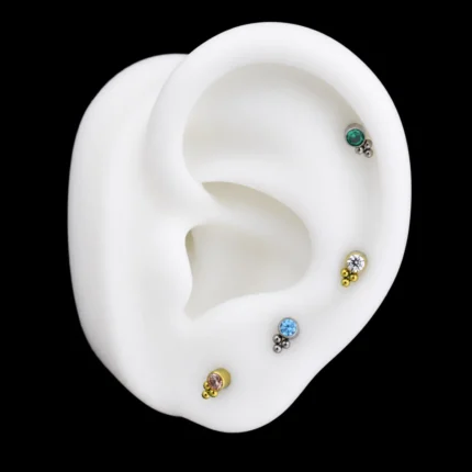 Tops con circón y tres bolitas en azul, blanco, verde y champaña puestos en una oreja de maqueta