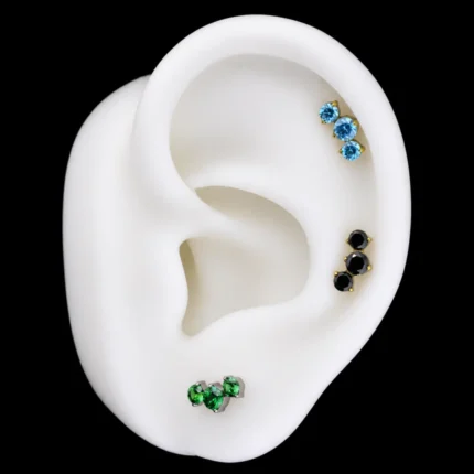 Tops de tres circones azul, negro y verde puestos en hélix y lóbulo de una oreja de maqueta