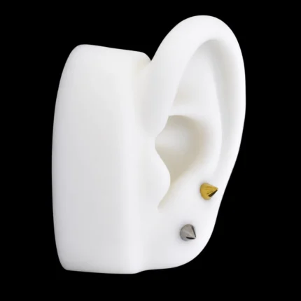 Tops de punta cónica dorado y plateado puestos en el lóbulo de una oreja de maqueta